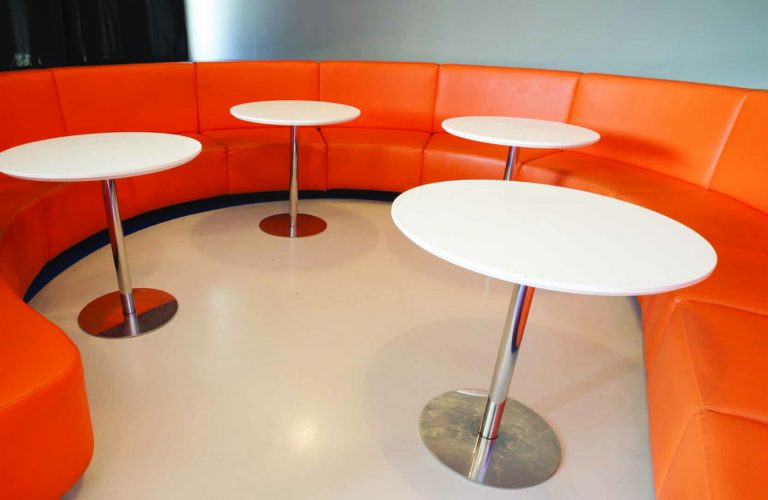 Powder coated orange bench with round pedestal tables.